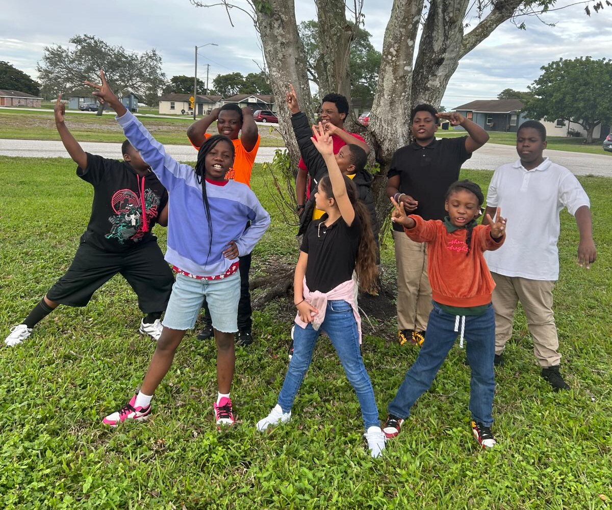 Children raising their hands together beside a tree during an outdoor Federation youth activity